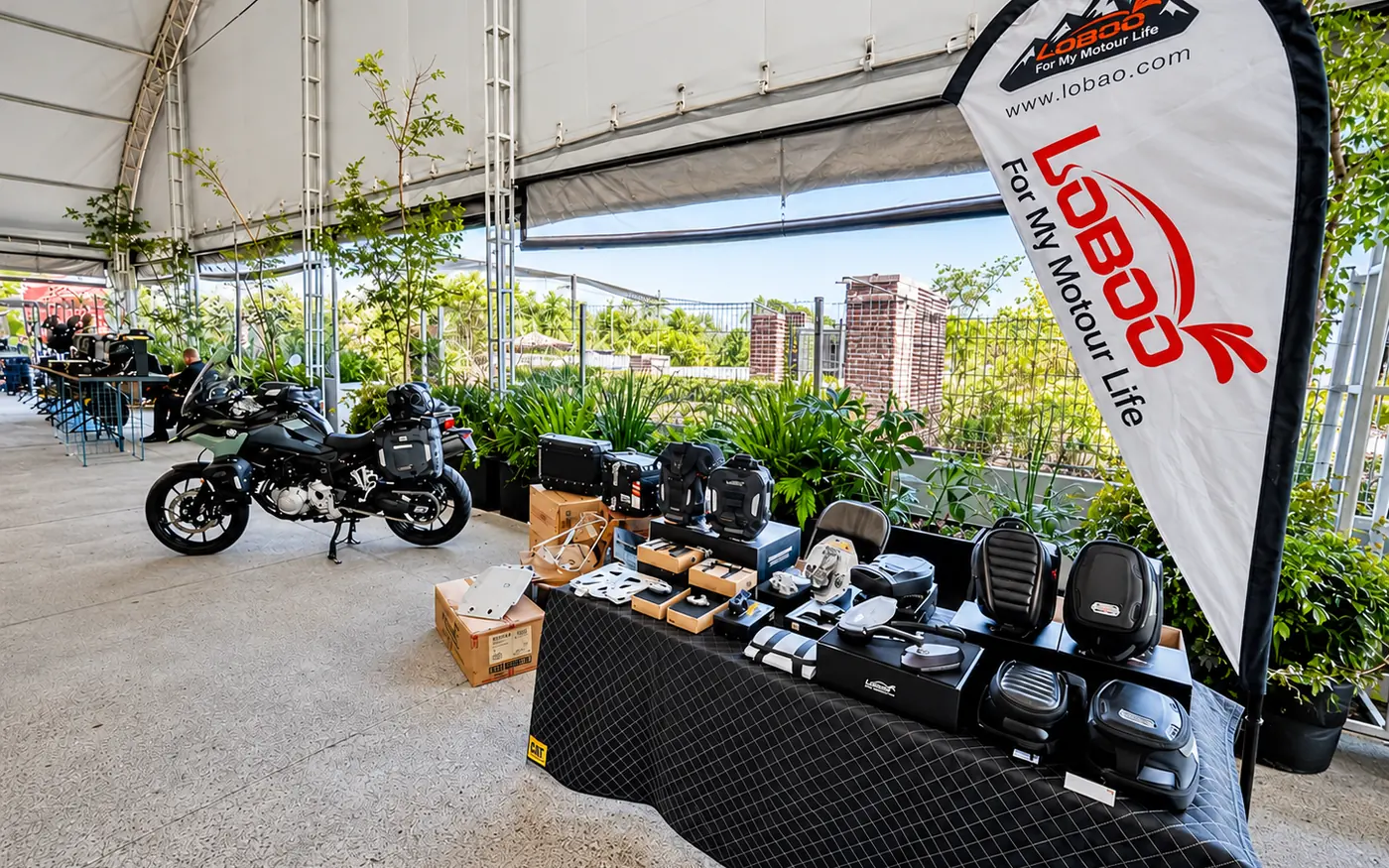 Stand de LOBOO con maletas, bolsas y accesorios junto a una moto adventure en el Open House Steel Protection